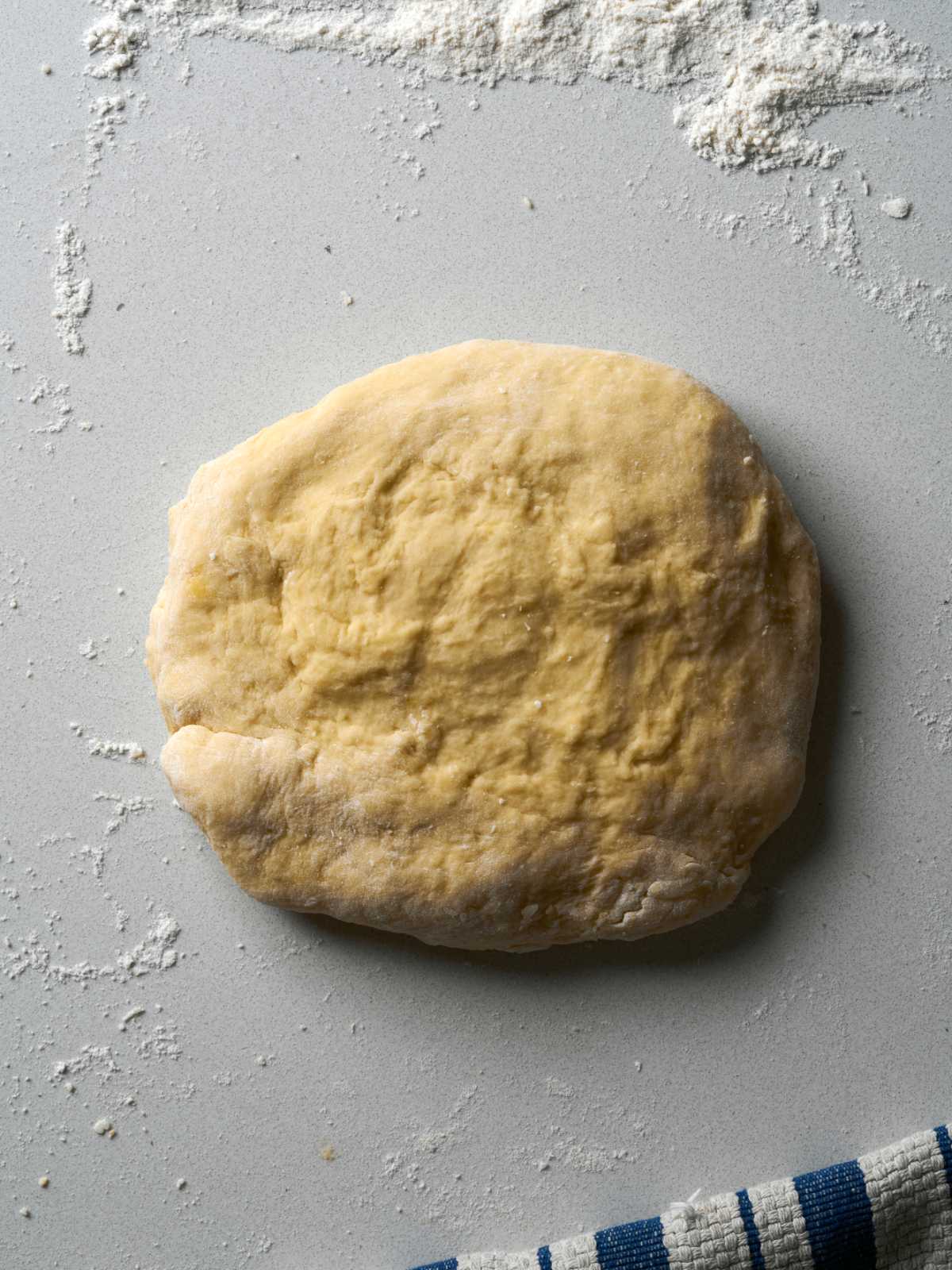 Disc of dough on a countertop next to a striped dish towel.