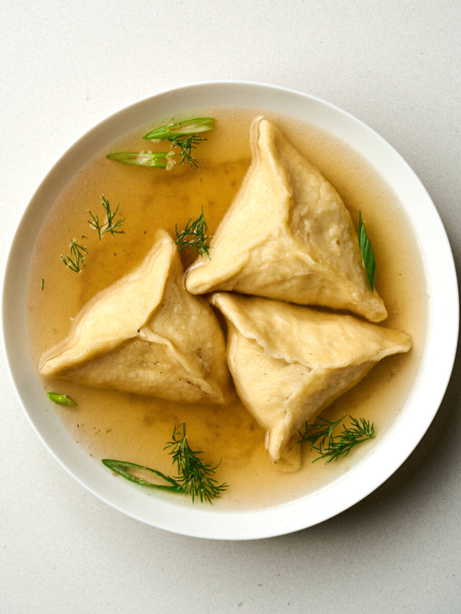 Top view of triangular dumplings in chicken broth with fresh herbs.