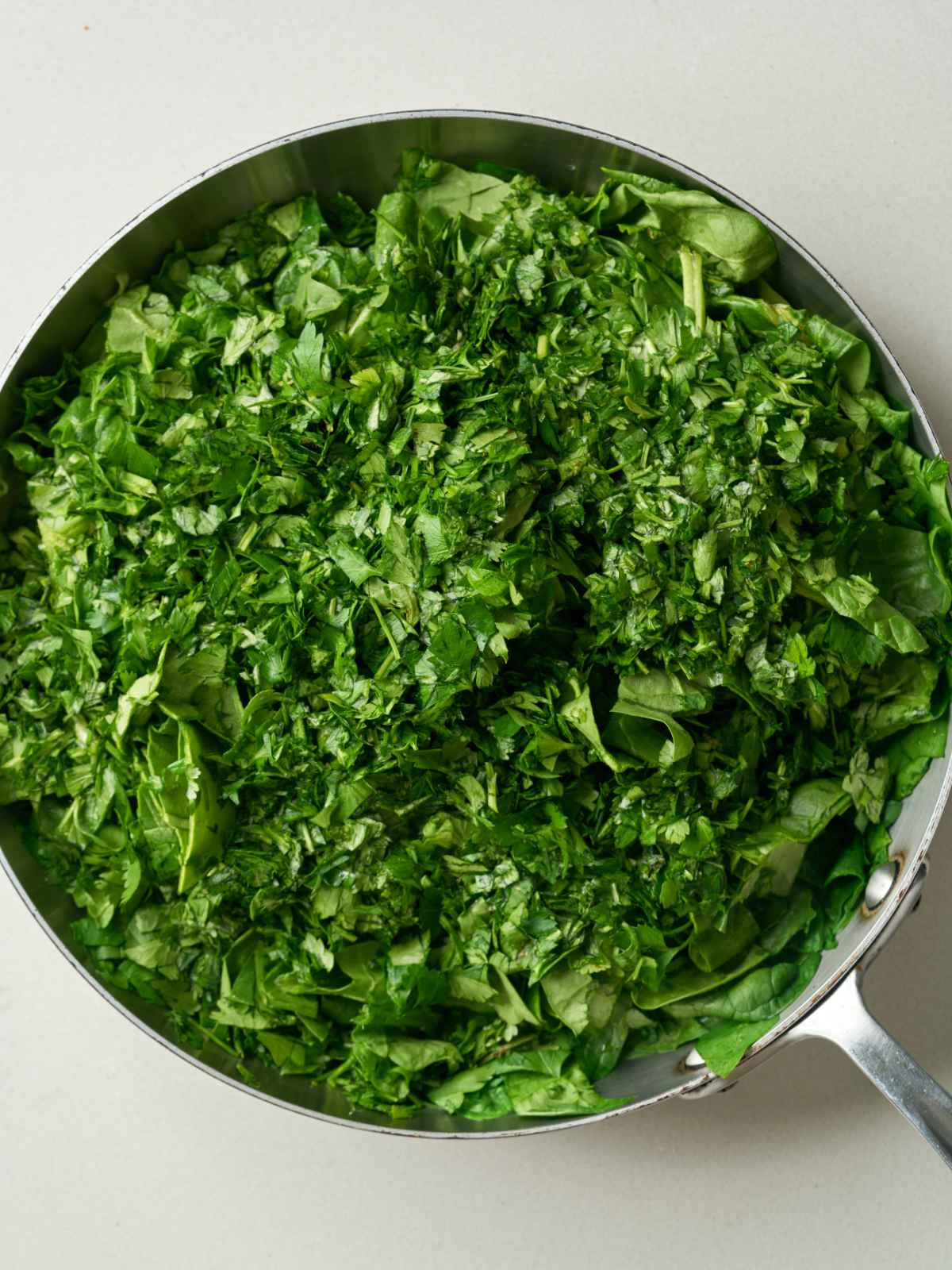 A saute pan with a large pile of fresh herbs