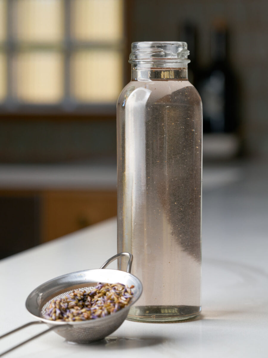 Glass bottle filled with simple syrup next to a small strainer with lavender flowers.