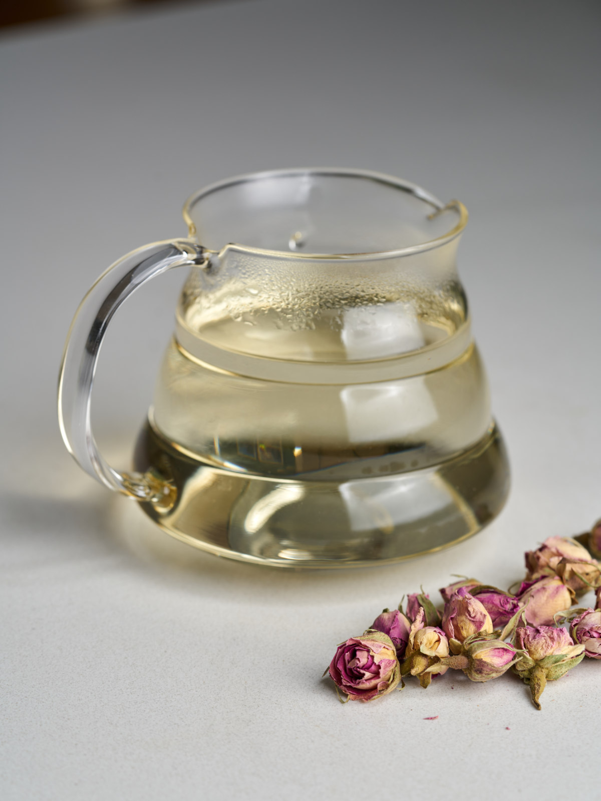 A glass pitcher with yellow simple syrup next to dried rose petals.