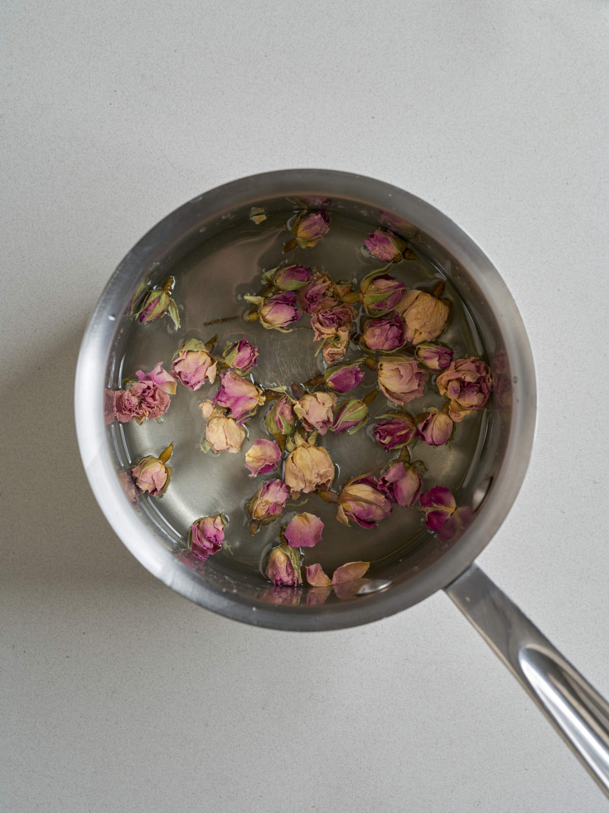 A metal saucepan with clear liquid and dried rose petals.