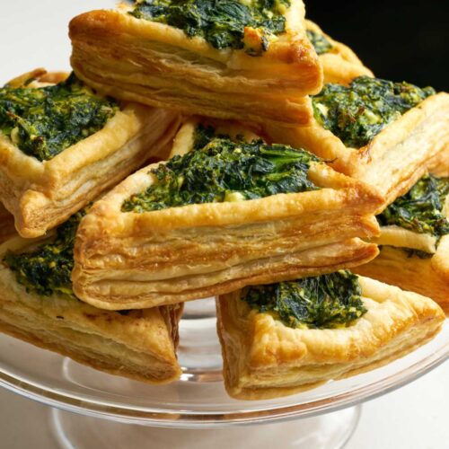 Triangular puff pastry tarts on a glass pedestal and filled with green filling.