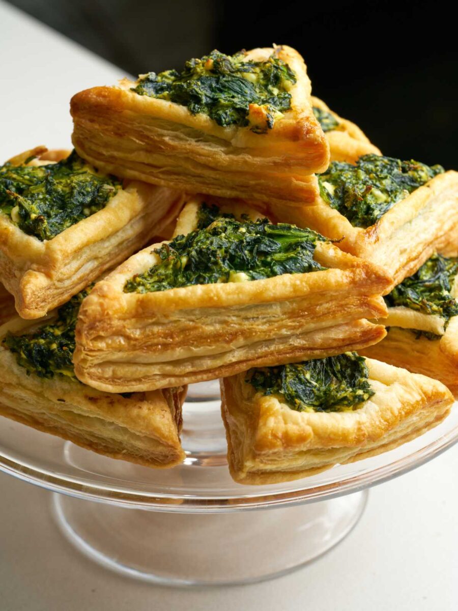 Triangular puff pastry tarts on a glass pedestal and filled with green filling.