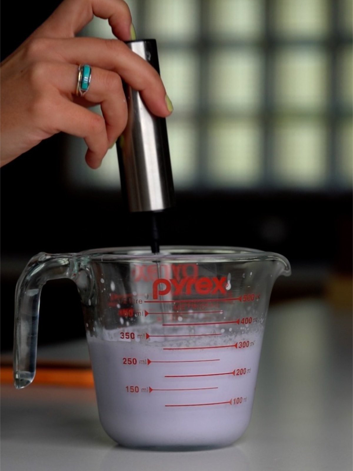 Frothing purple foam in a liquid measuring cup with a handheld frother.