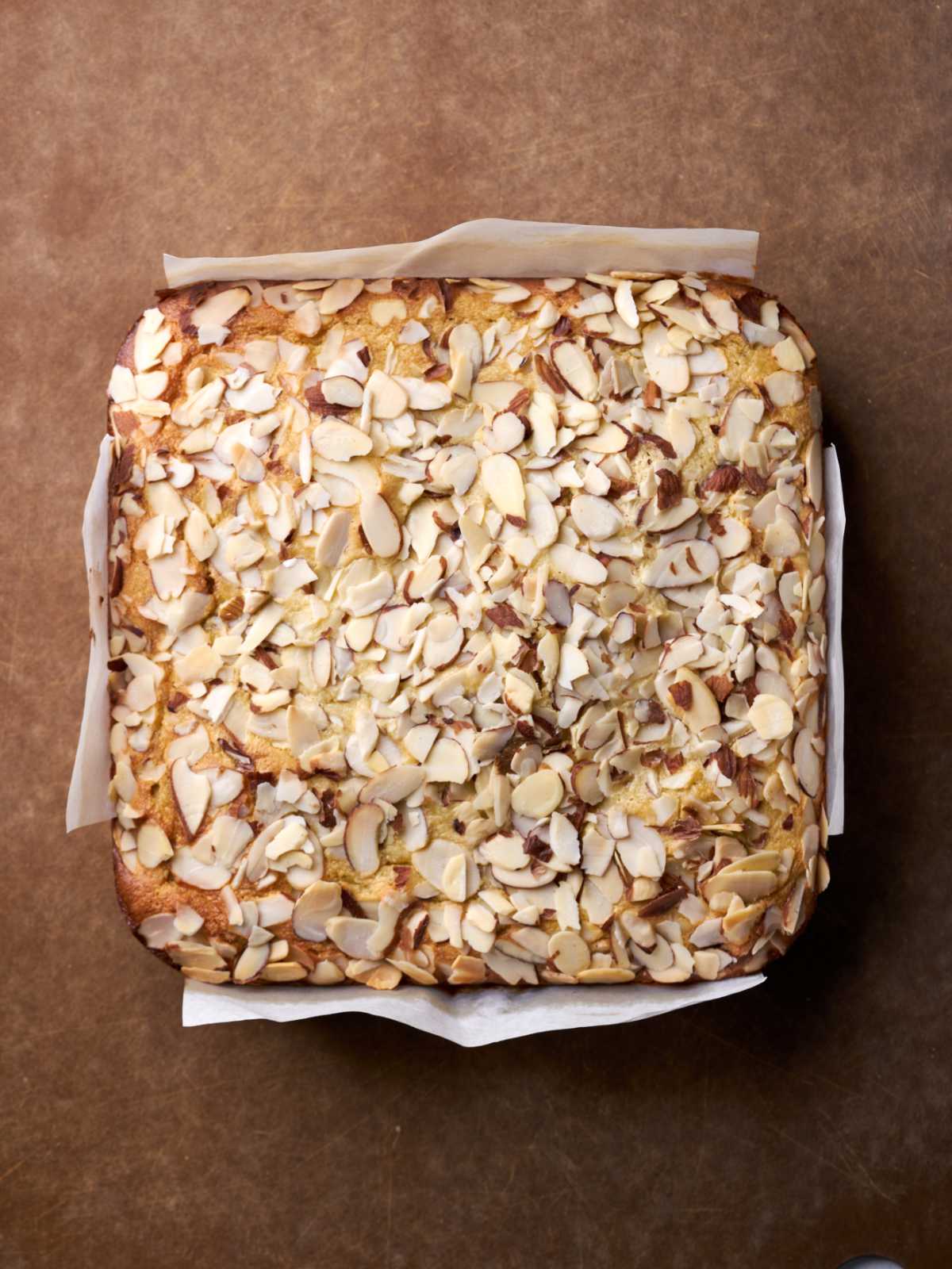 Top down view of a square cake with an almond topping wrapped in parchment paper