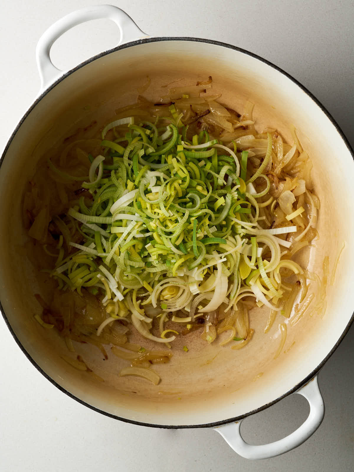 Caramelized onions in a large white pot topped with freshly sliced scallions.