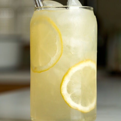 Lemonade in a soda can glass with lemon slices next to lavender buds.