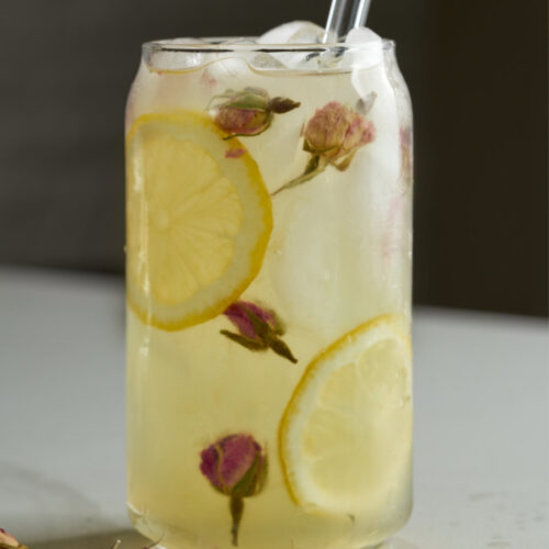 Lemonade in a soda can glass with lemon slices and dried rose buds.