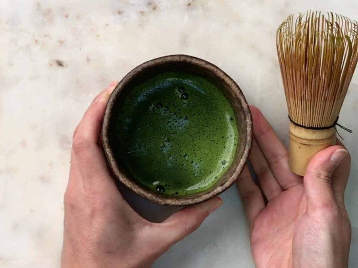 Hands holding whisked green tea in a bowl.