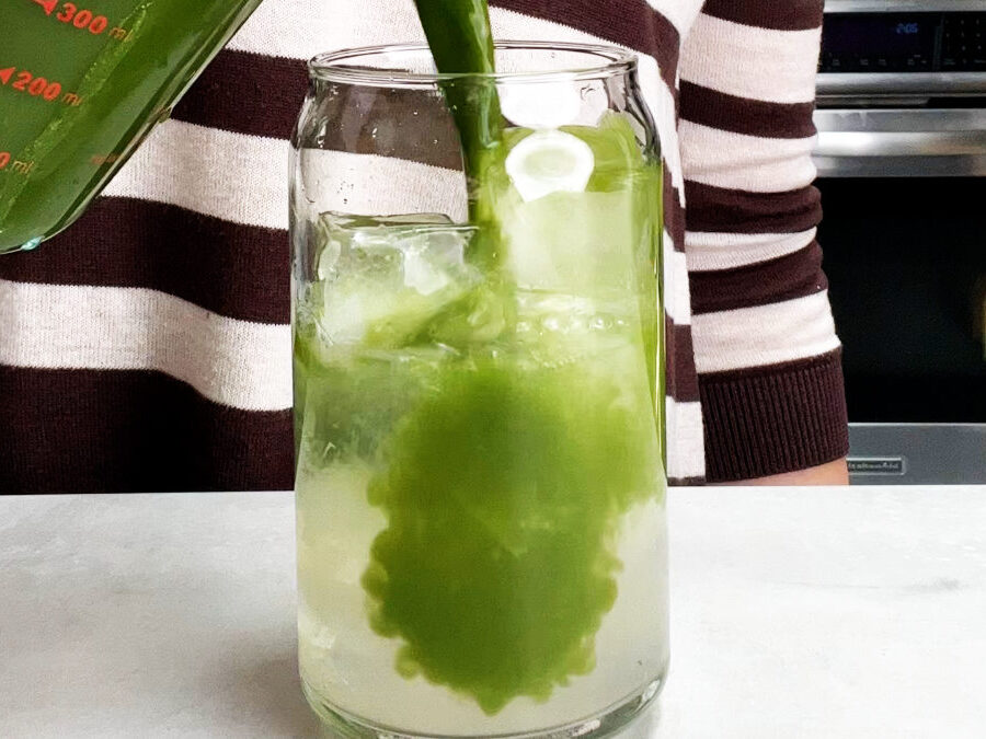 A woman in a stripy shirt pouring green tea into a glass of water and ice.