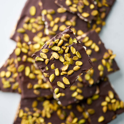 A pile of square pieces of matzo with chocolate and pistachios