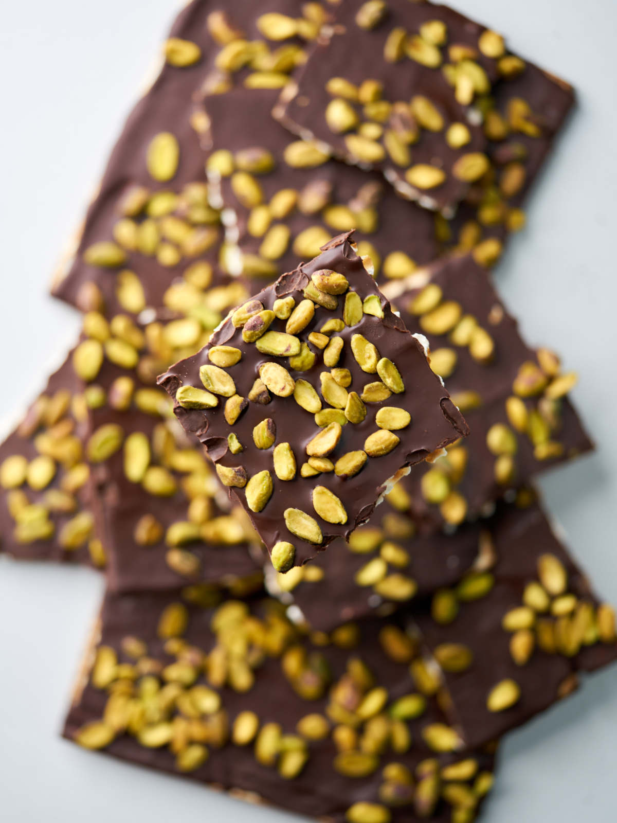 A pile of square pieces of matzo with chocolate and pistachios