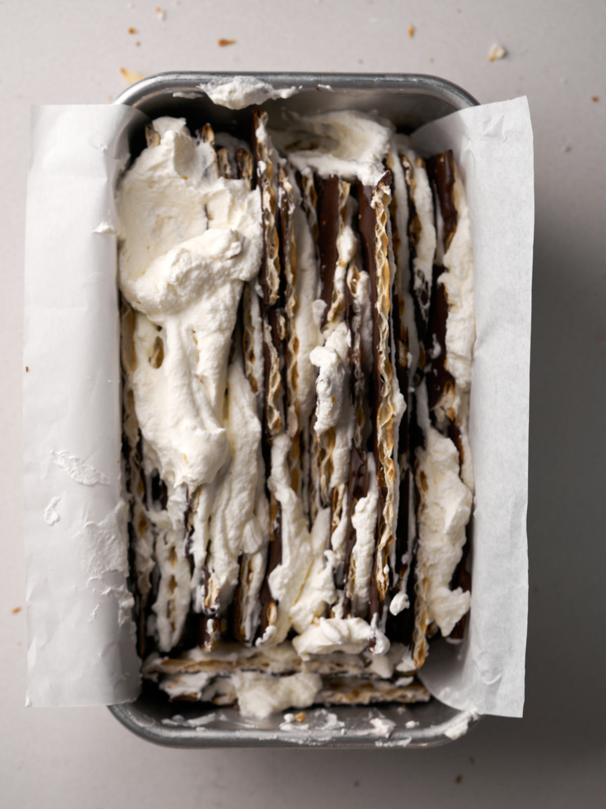 Vertical layers of matzo, chocolate and whipped cream in a silver loaf tin lined with parchment.