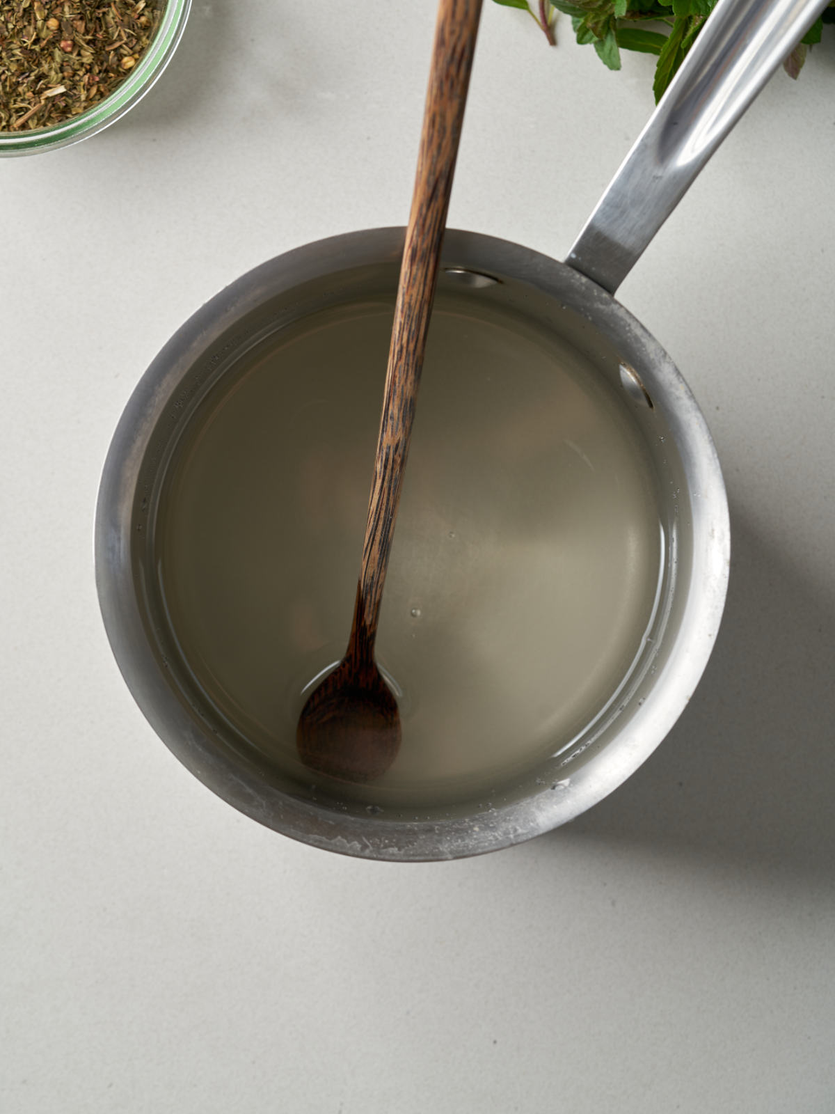 Simple syrup in a saucepan with a skinny wooden spoon.