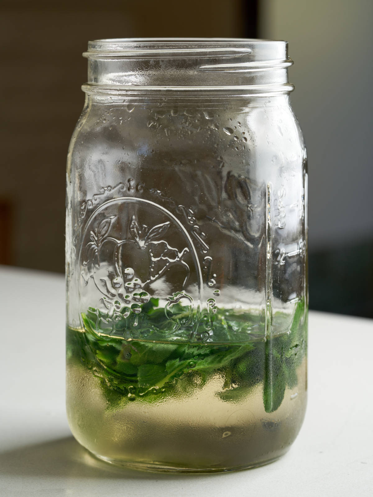 Simple syrup and mint leaves in the bottom half of a quart mason jar.