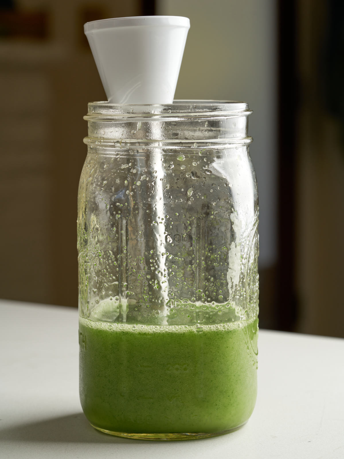 Green liquid in a quart mason jar with the bottom of an immersion blender resting inside.