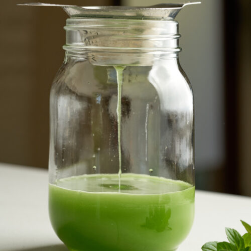 Green liquid drizzling into a glass mason jar.
