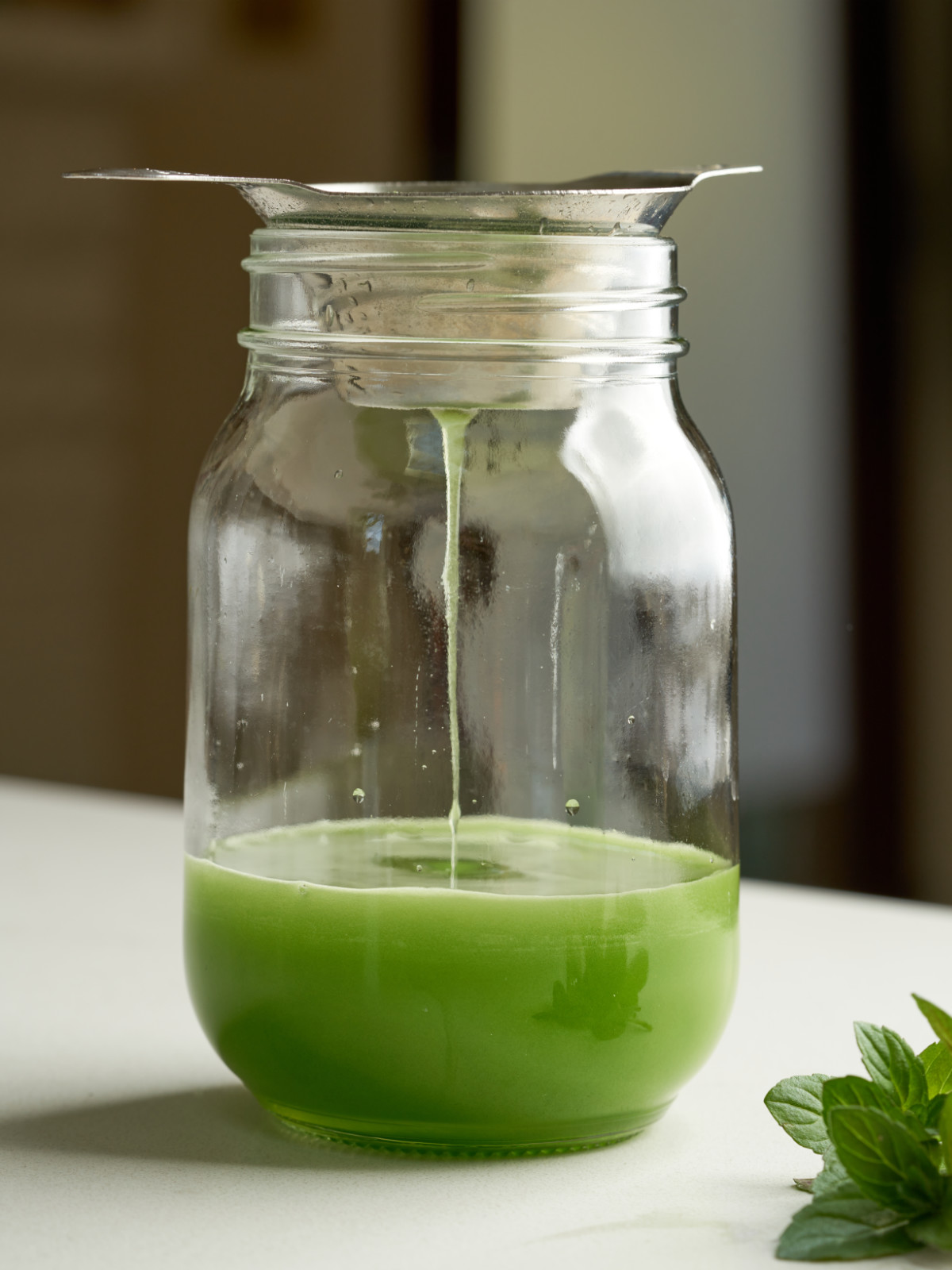 Green liquid drizzling through a strainer into a glass mason jar.