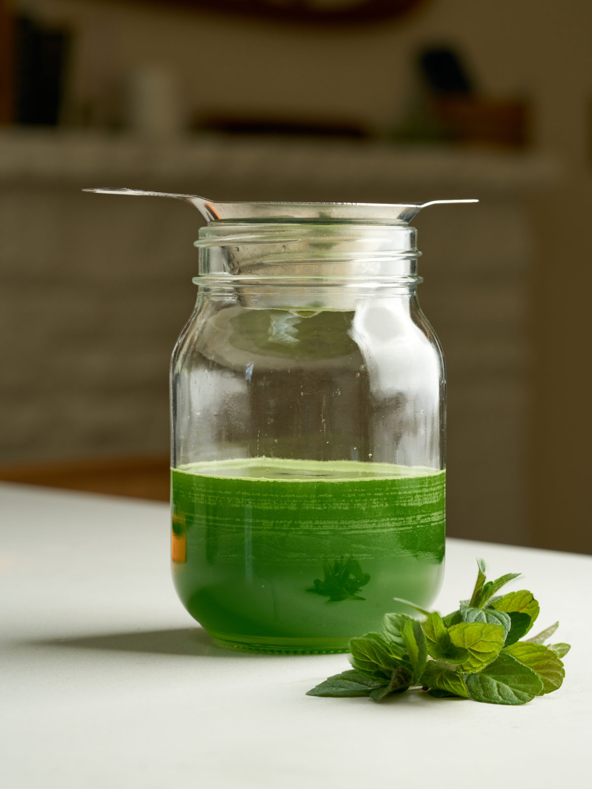 Green liquid drizzling into a glass mason jar through a metal mesh strainer.