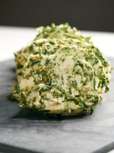 Large circles of green and beige butter on a cutting board.