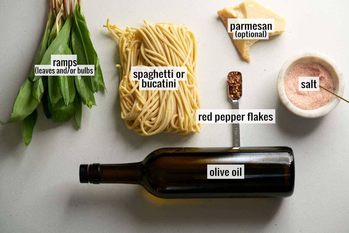 Ramp leaves next to homemade pasta, a bottle of olive oil, salt, red pepper flakes, and a wedge of parmesan.