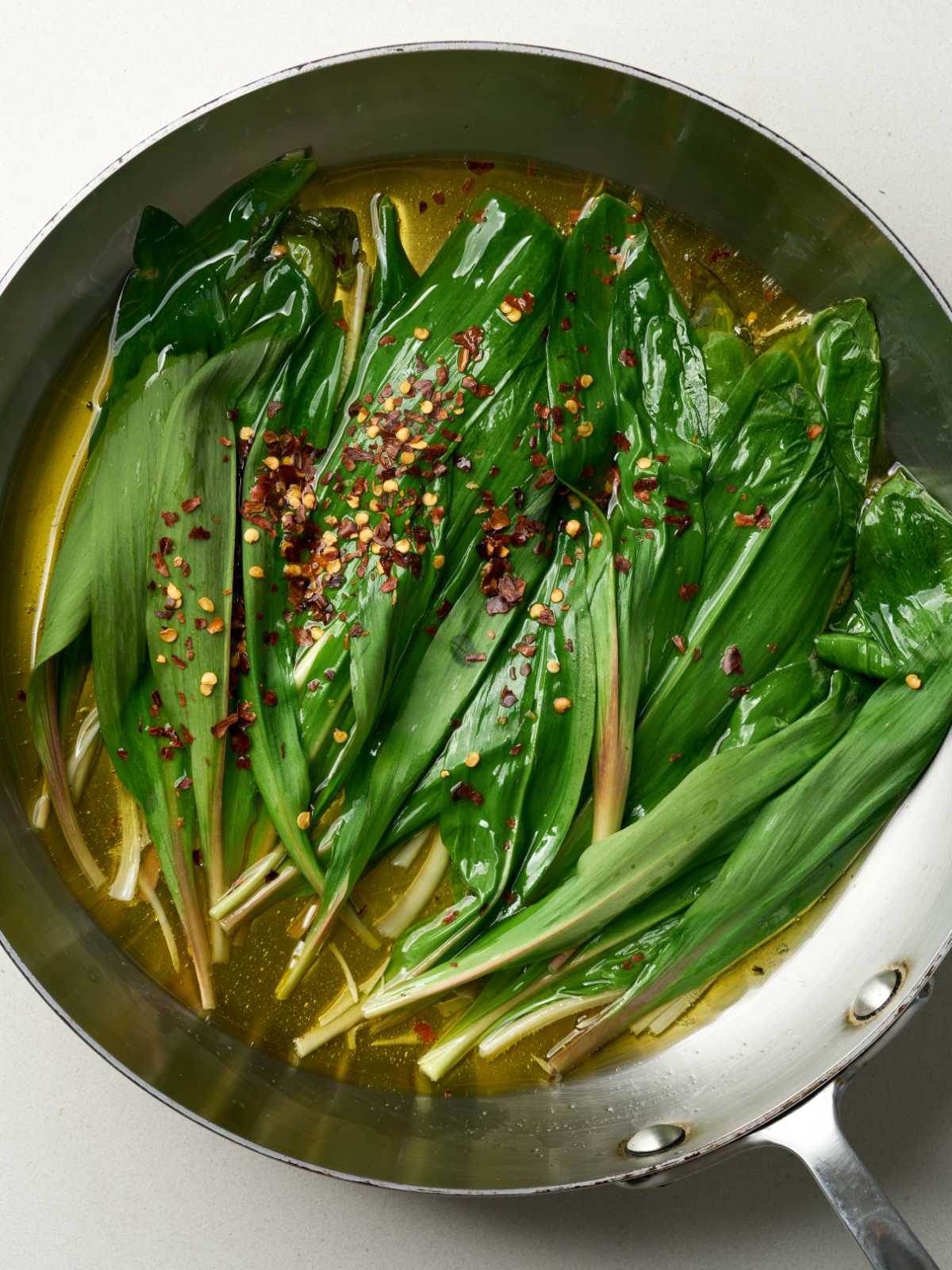 Green ramps cooking in oil in a large silver saucepan