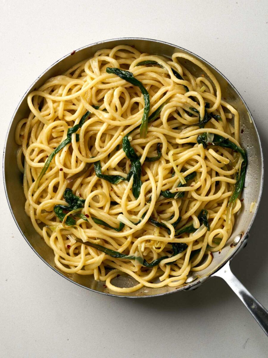 Cooked bucatini pasta with greens in a large silver sauce pan.