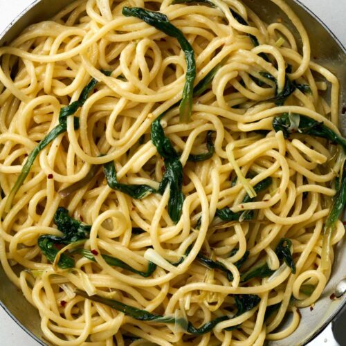 Cooked bucatini pasta with greens in a large silver sauce pan.