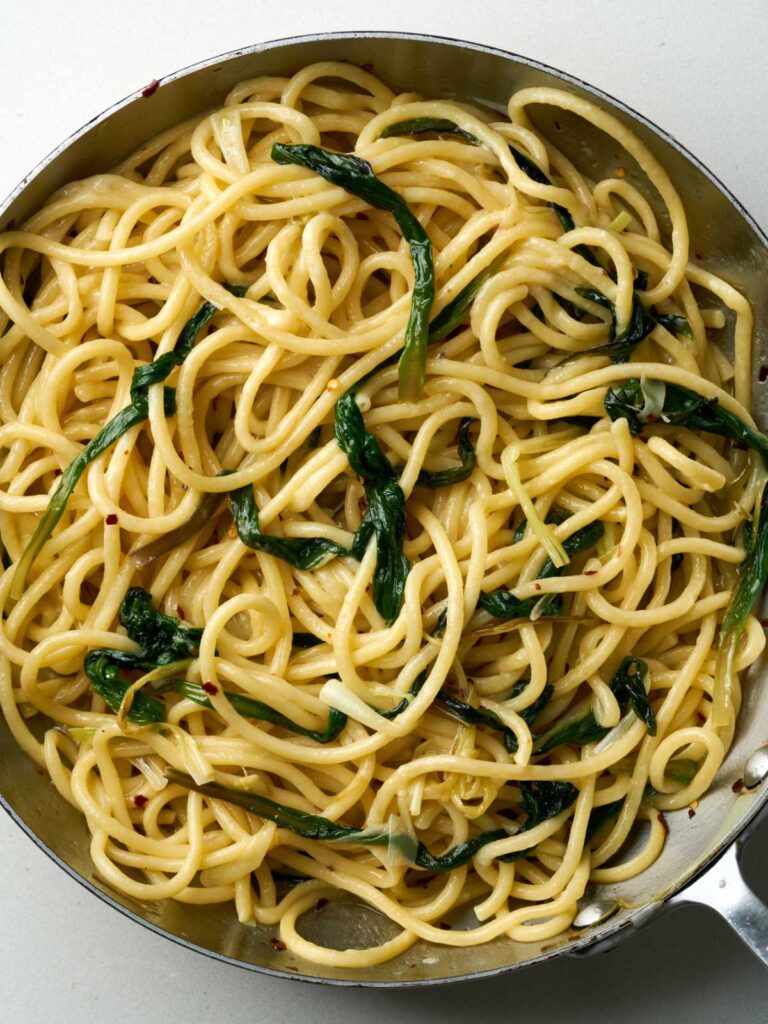 Cooked bucatini pasta with greens in a large silver sauce pan.