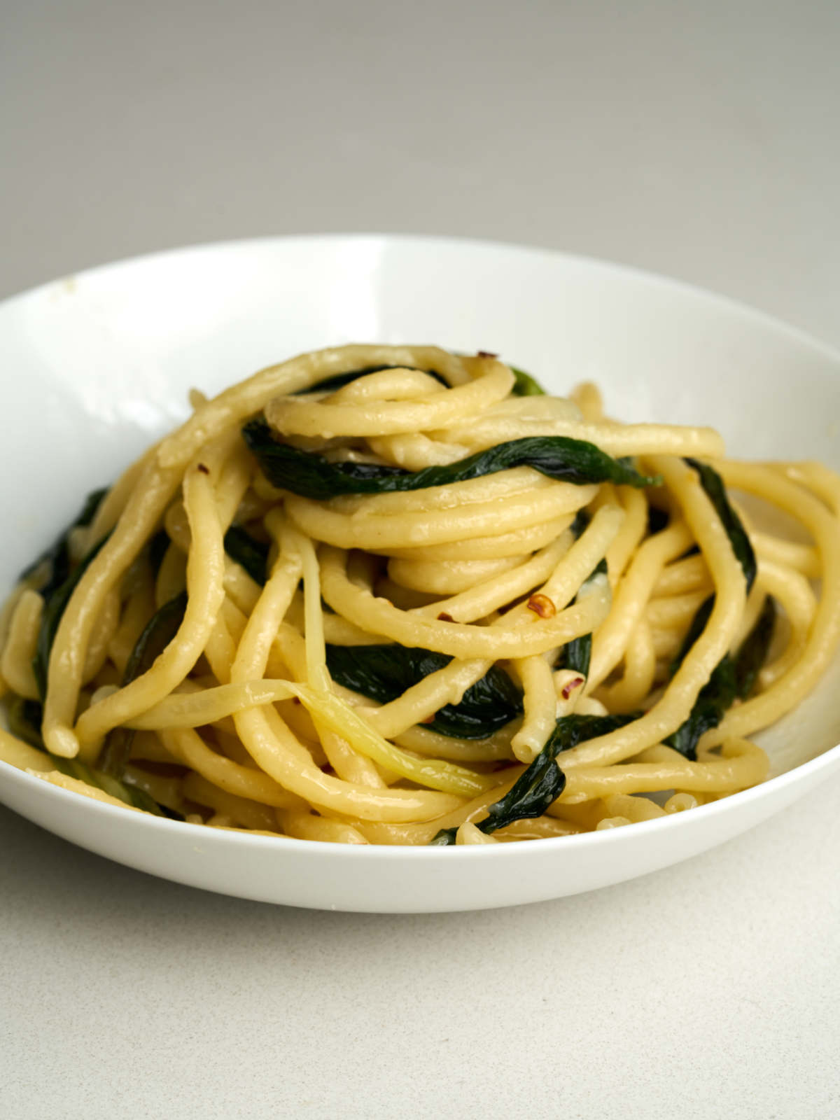 Bucatini pasta with greens in a white bowl.