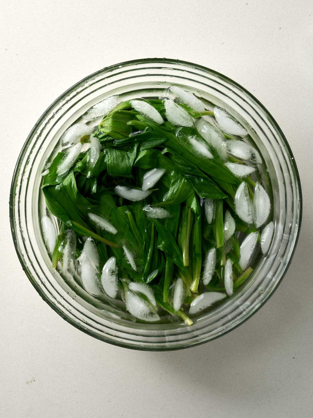 Green leaves submerged in an ice bath in a glass bowl.