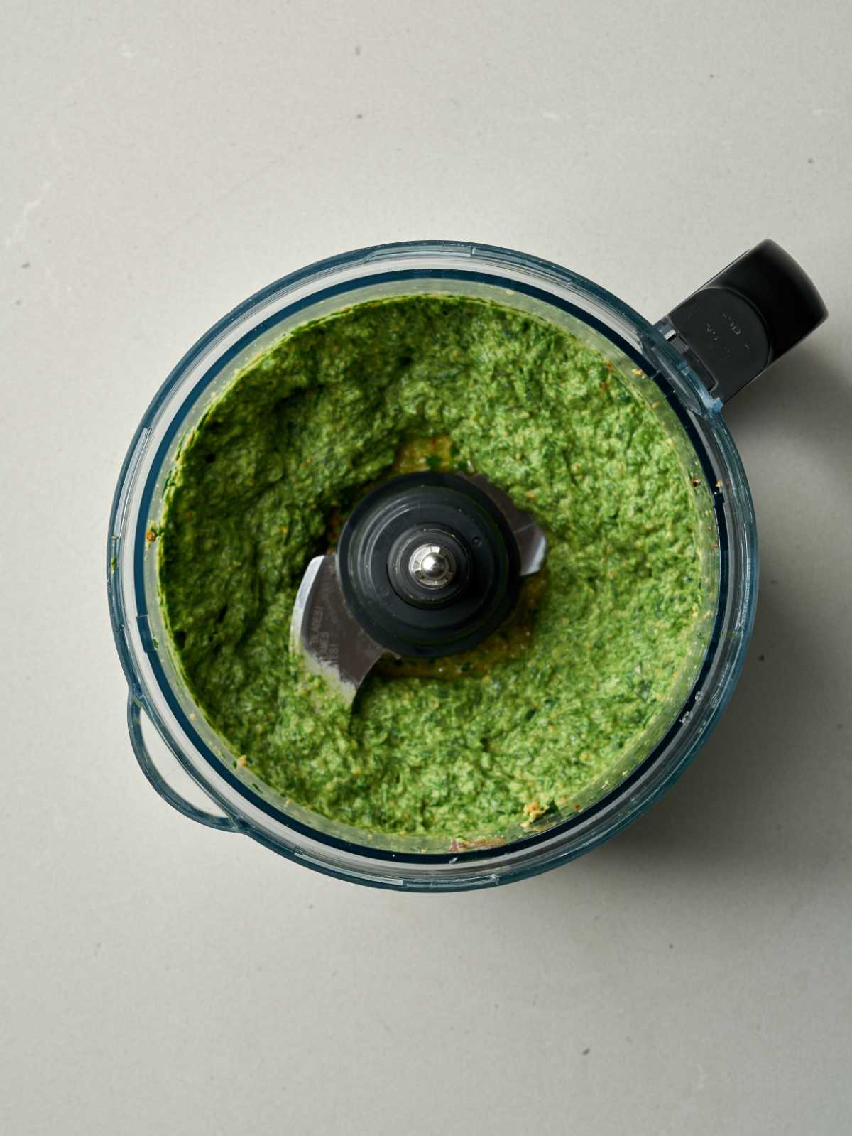 Blended green pesto in a food processor with a black handle.