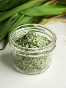 Side view of green and white salt in a small glass jar with leaves behind