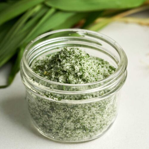 Side view of green and white salt in a small glass jar with leaves behind