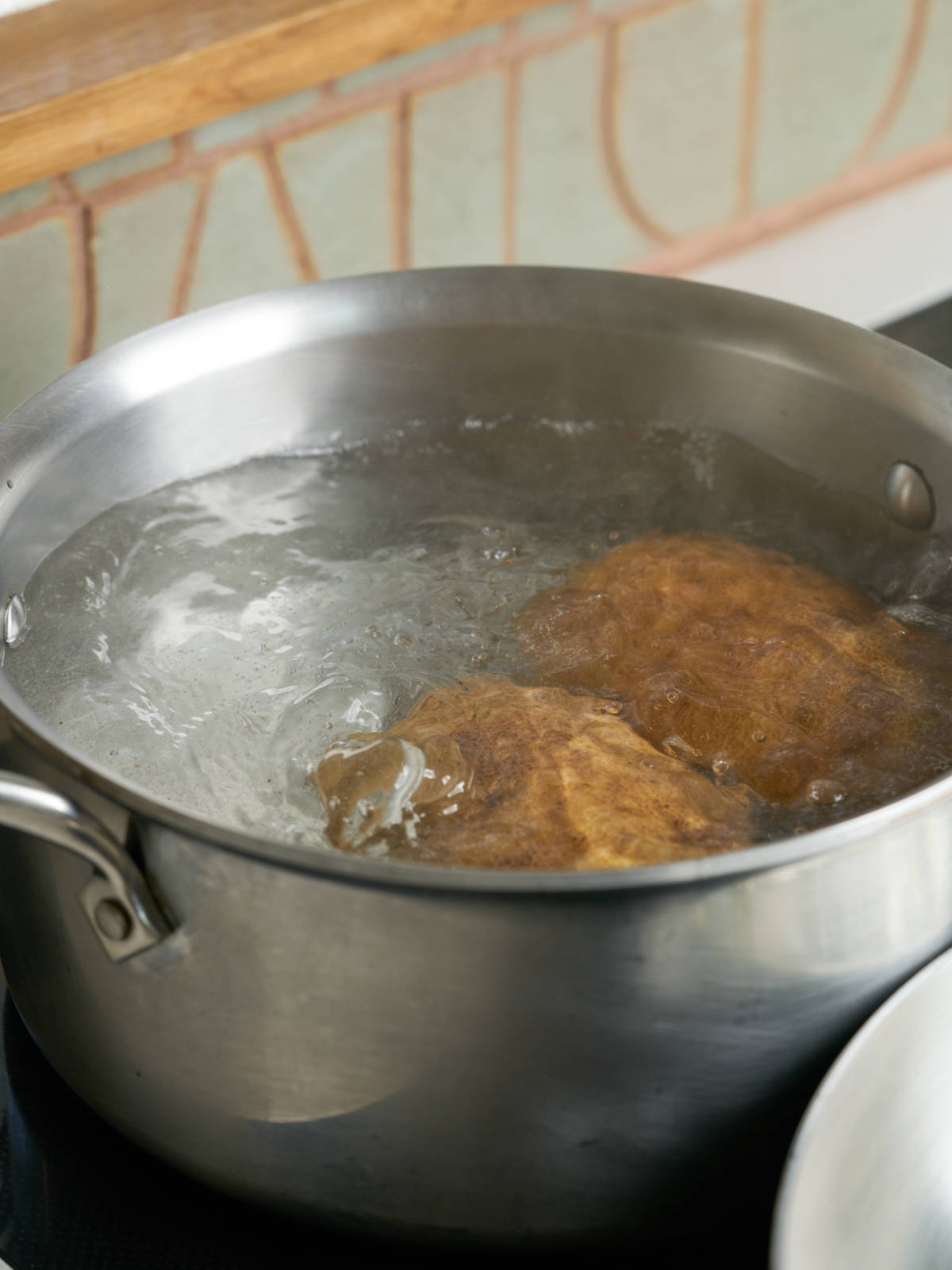 Potatoes boiling in hot water in a large silver saucepan.