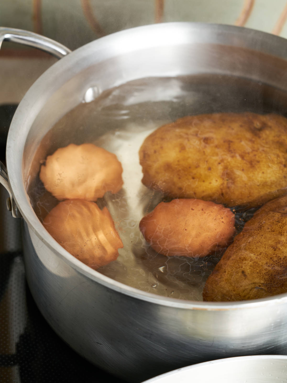 Potatoes and eggs submerged in water in a large silver saucepan.