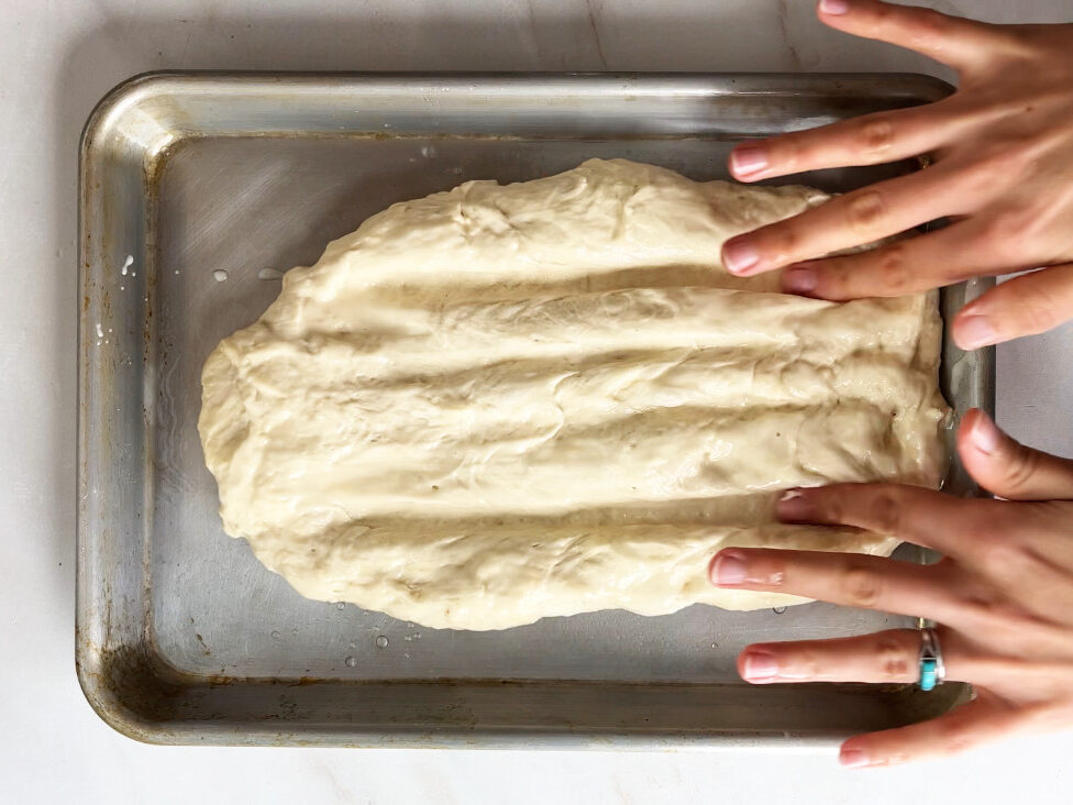 Fingers making grooves in dough on a baking sheet.