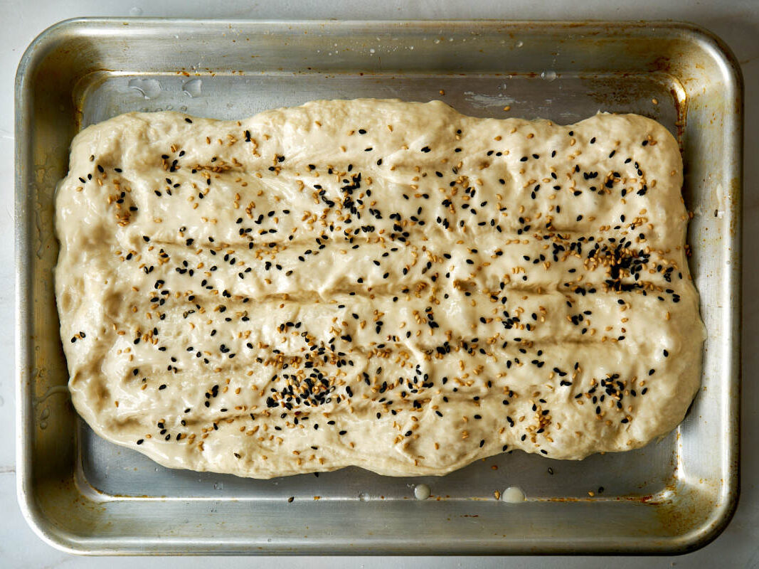 Dough with sesame seeds on a baking sheet.
