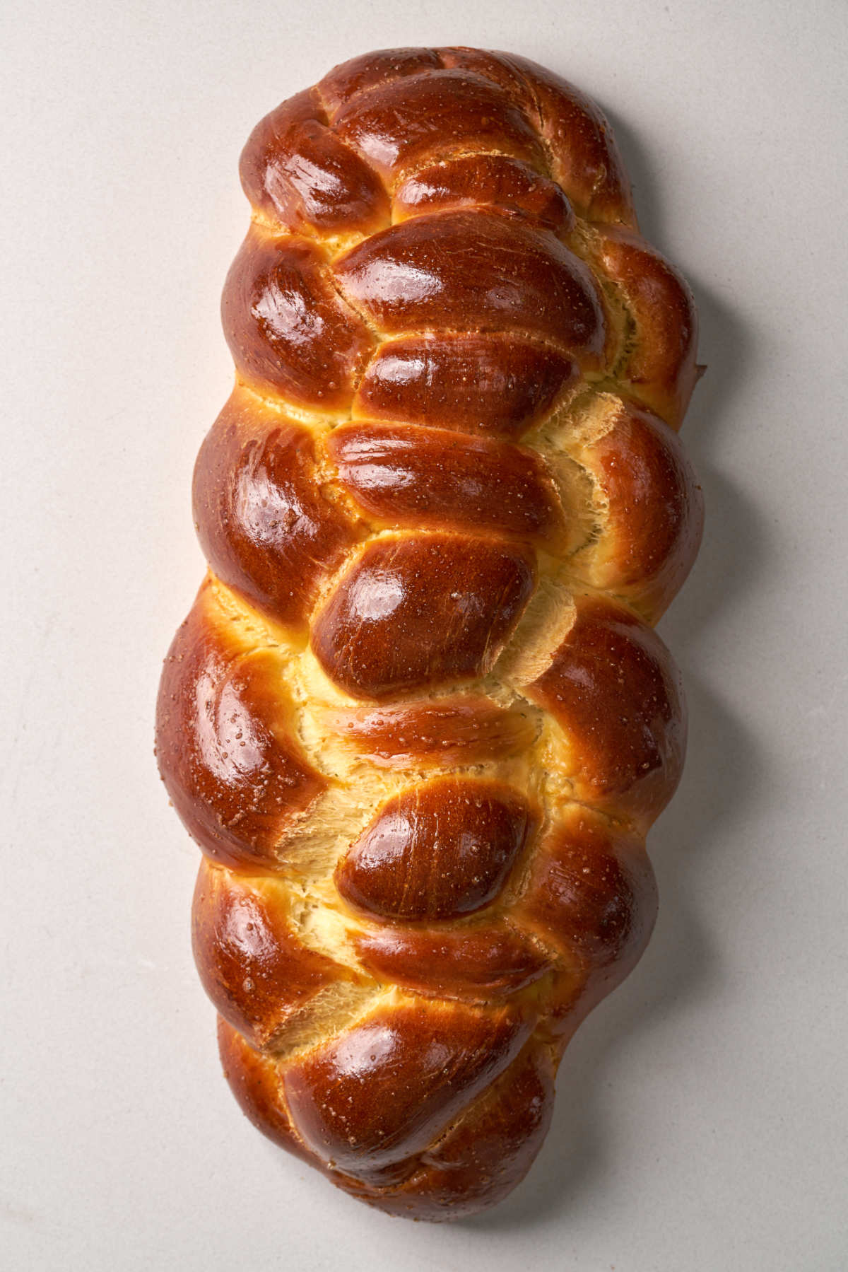 A brown, baked, braided challah bread on a white background.