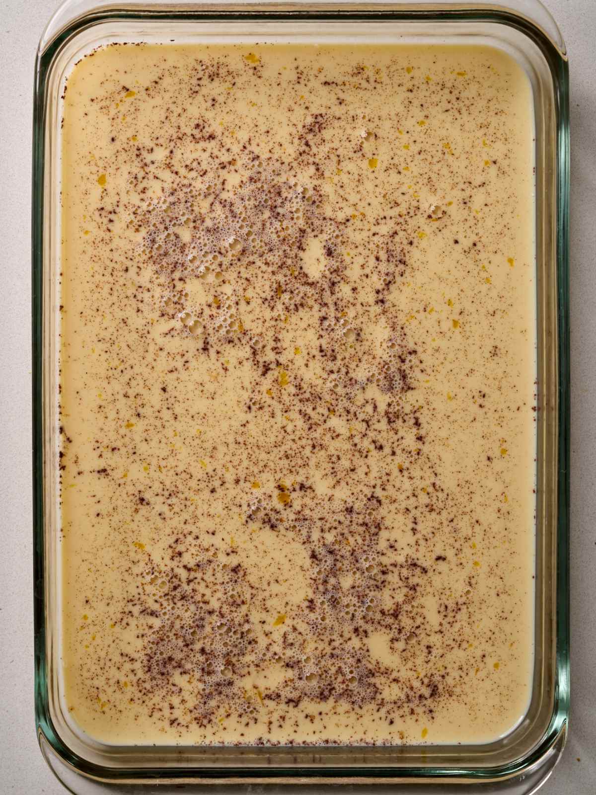 A large glass baking dish containing a light brown liquid with flecks of spices.