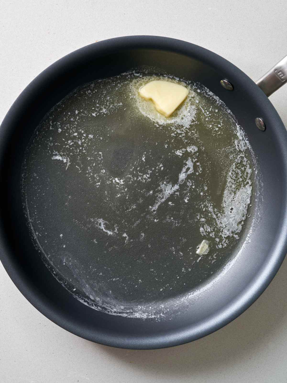 A knob of butter melting in a shiny black pan.