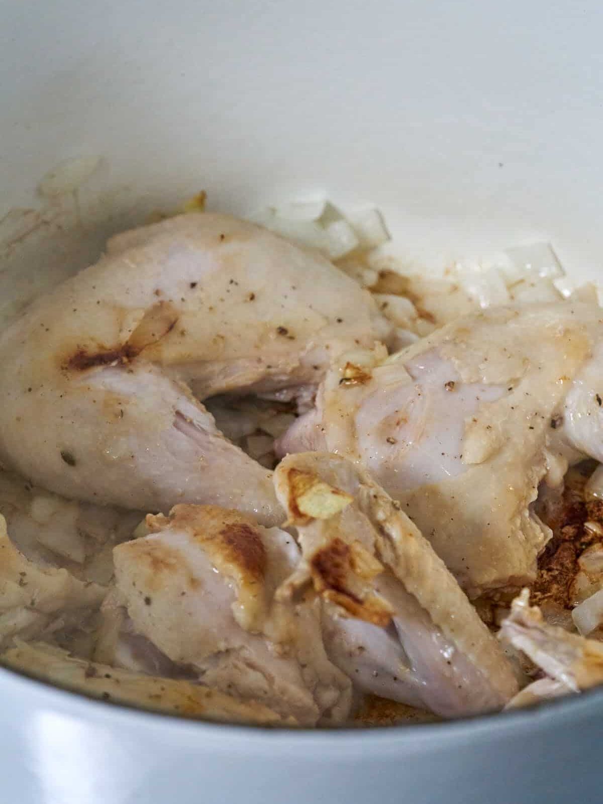 Browned chicken in a pot with onions.