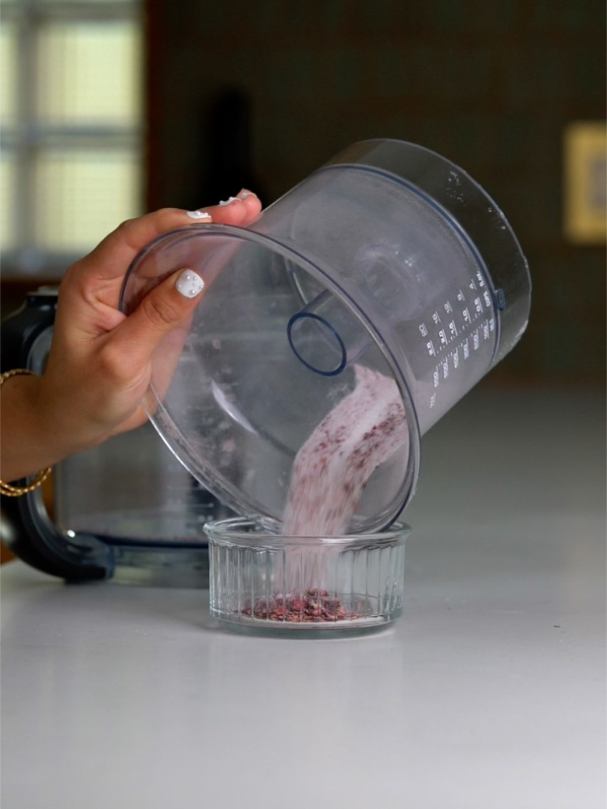 A hand pouring pink sugar out of a large food processor container.