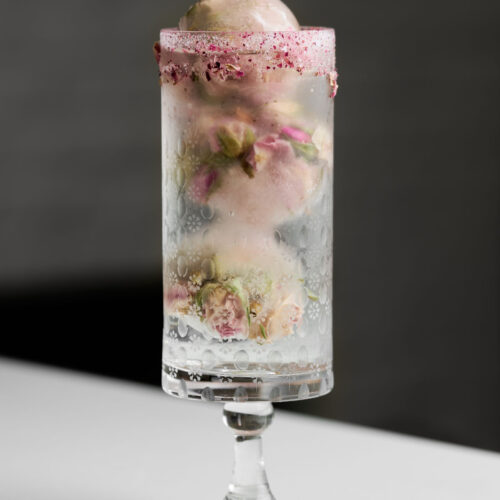 Rose bud ice cubes in a cocktail glass with a pink sugar rim.