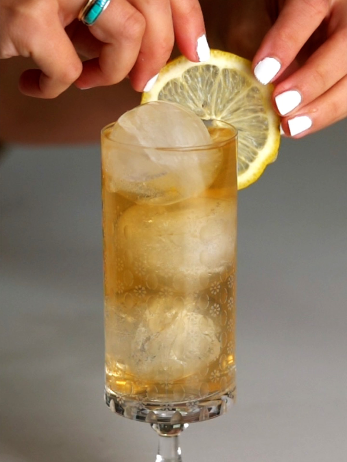 Fancy drink in a pedestal glass with two hands adding a lemon slice garnish.