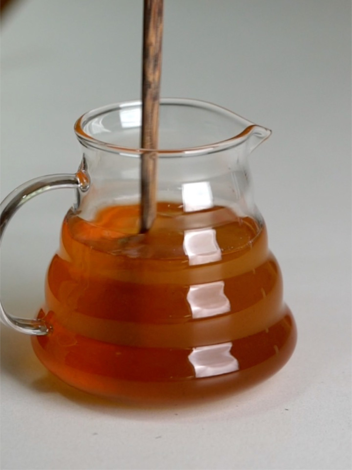 Rust colored liquid in a glass pitcher with a wooden spoon.