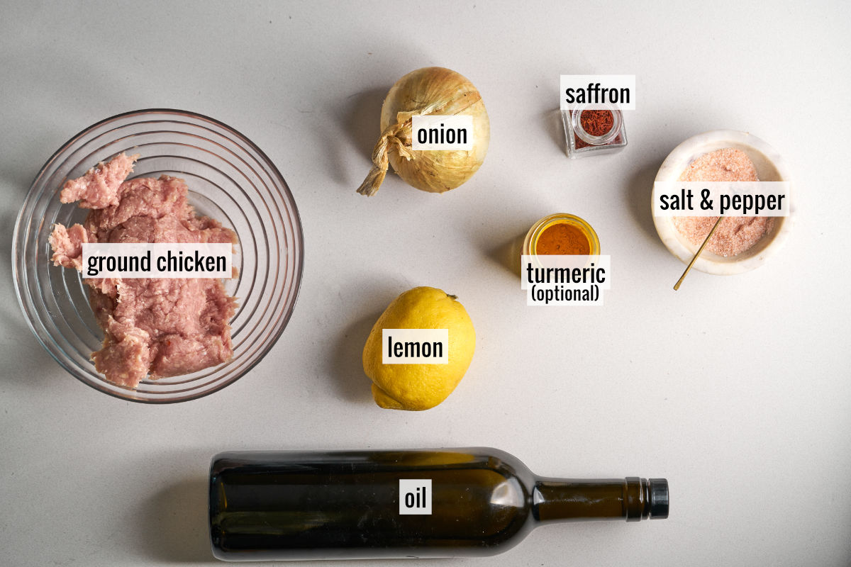 Ground chicken, a lemon, an onion, spices, and a bottle of oil on a countertop.