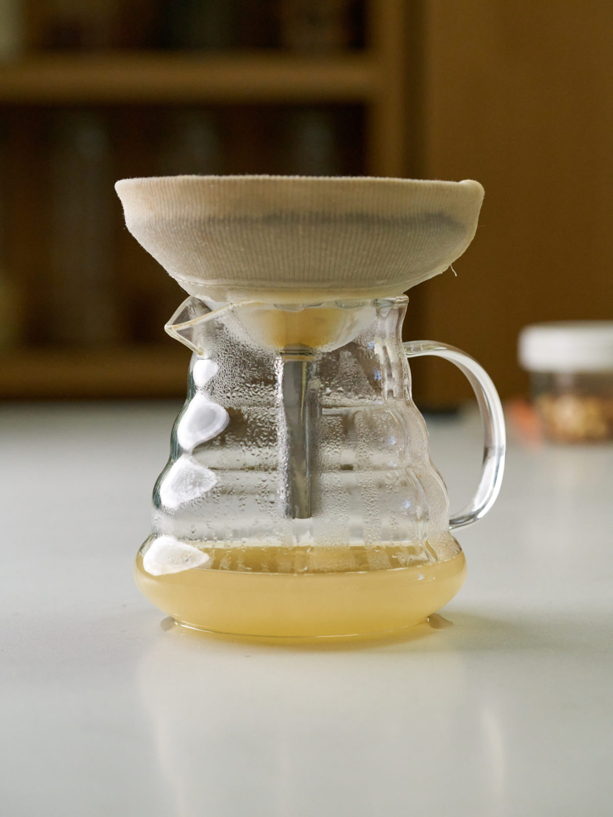 Funnel on top of a glass pitcher with yellow juice.