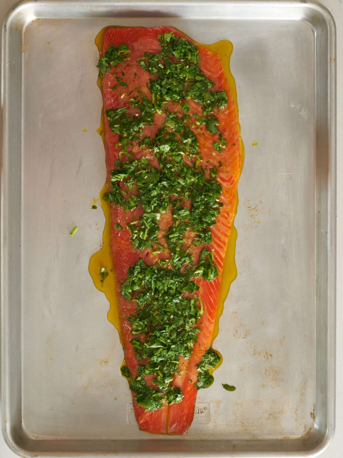 Raw salmon on a baking sheet covered in herbs and yellow sauce.